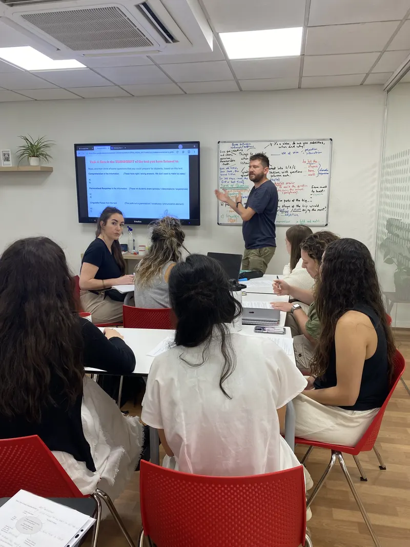Una clase de inglés en grupo en nuestra escuela de Barcelona: el profesor explica en la pizarra mientras los alumnos siguen la actividad