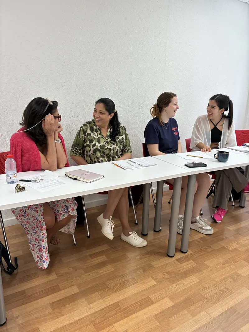 Alumnos adultos conversando en inglés alrededor de la mesa durante una clase en grupo reducido